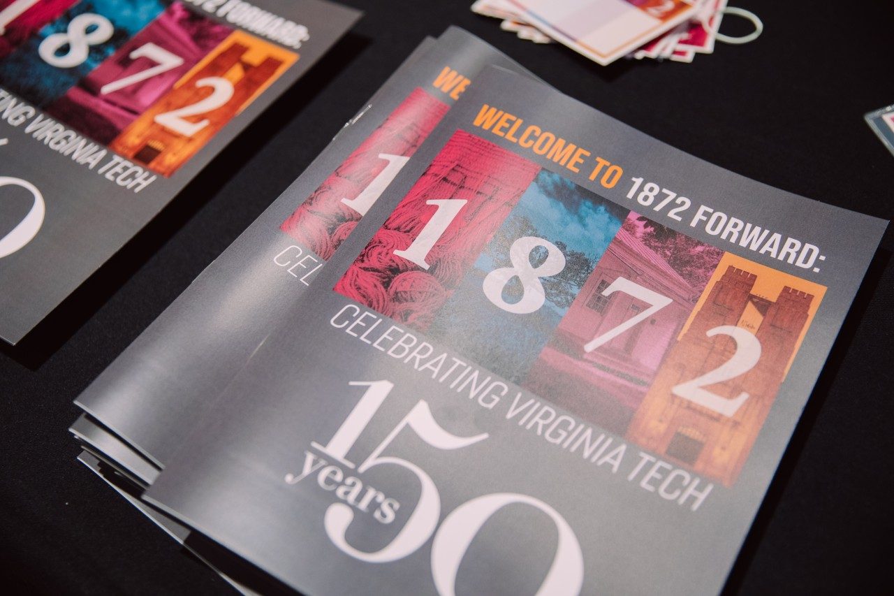 A pile of programs for the event are stacked on the table. The front of the program reads: Welcome to 1872 Forward: Celebrating Virginia Tech. 